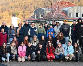 Eine Gruppe von etwa 40 Personen steht im Freien, umgeben von Bäumen und Gebäuden, und posiert für ein Gruppenfoto.