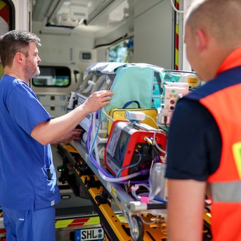 Ein Rettungssanitäter und ein Arzt bringen eine Trage mit medizinischer Ausrüstung in einen Krankenwagen.