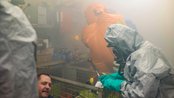 Ein Rettungsteam in Schutzanzügen hilft einer Person in einem verrauchten Raum, während Ausrüstung im Hintergrund sichtbar ist.