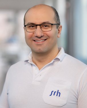 Ein Mann mit Brille trägt ein weißes Polohemd mit dem Logo "srh" auf der Brust. Er lächelt freundlich in die Kamera.