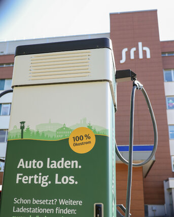 Ladestation für Elektroautos mit dem Hinweis "100% Ökostrom" und der Aufforderung "Auto laden. Fertig. Los." im Vordergrund.