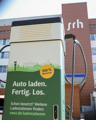 Ladestation für Elektroautos mit dem Hinweis "100% Ökostrom" und der Aufforderung "Auto laden. Fertig. Los." im Vordergrund.