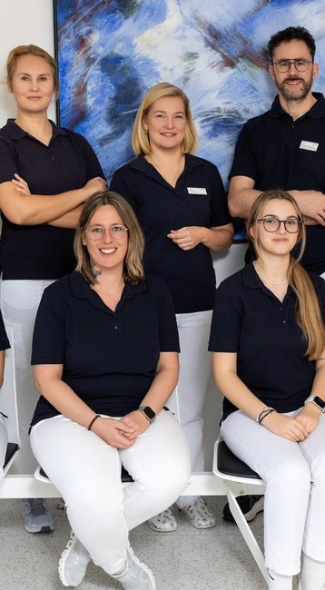 Eine Gruppe von zwölf Personen in blauen Poloshirts und weißen Hosen, die in einem modernen Raum posieren.