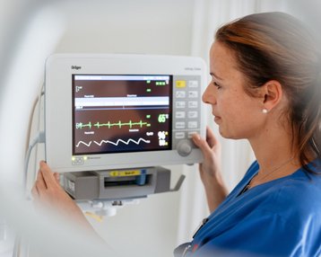 Eine Krankenschwester überprüft einen Patientenmonitor in einem Krankenhaus, während sie die Vitalzeichen auf dem Bildschirm betrachtet.