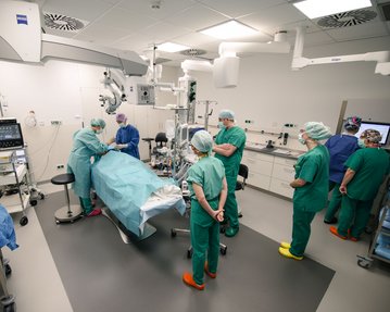 Ein Operationsteam in grüner Kleidung führt einen Eingriff an einem Patienten auf einem Operationstisch in einem modernen Operationssaal durch.