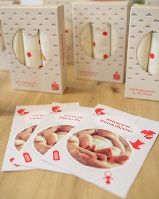 Geschenkpäckchen mit bunten Designs und Karten, die "Willkommen kleines Wunder!" zeigen, liegen auf einem Tisch.