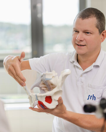 Ein Arzt erklärt einer Patientin die Anatomie des Beckens mit einem anatomischen Modell in einer Klinik.