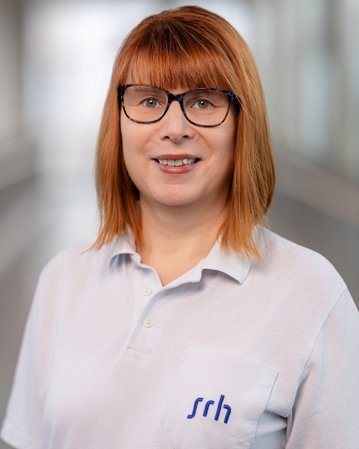 Frau mit rotem Haar und Brille trägt ein helles Poloshirt mit dem Logo "srh". Sie steht in einem modernen Innenraum.