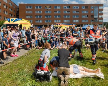 Rettungskräfte leisten Erste Hilfe an einer Person auf einer Liege, während eine Menschenmenge zuschaut. Im Hintergrund sind Rettungswagen und ein abgesperrter Bereich sichtbar.