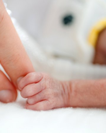 Ein zartes Babyhändchen greift nach dem Finger eines Erwachsenen, während es auf einer weichen Unterlage liegt.