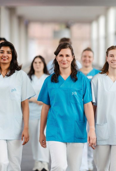Eine Gruppe von Pflegekräften in Uniform geht durch einen Krankenhausflur, einige tragen Infusionsständer.