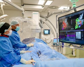 Zwei Ärzte in OP-Kleidung arbeiten an einem medizinischen Monitor, der farbige Daten anzeigt, während sie sich auf einen Patienten vorbereiten.