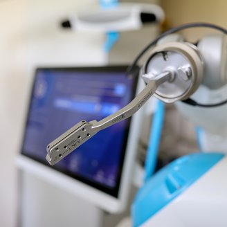 Ein chirurgischer Roboterarm mit einem präzisen Instrument, im Hintergrund ein Monitor mit medizinischen Informationen.