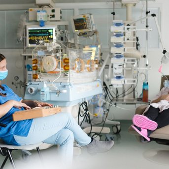 Eine Krankenschwester spielt ein Instrument, während eine Mutter mit ihrem Baby in einem Krankenhauszimmer sitzt. Medizingeräte sind im Hintergrund sichtbar.