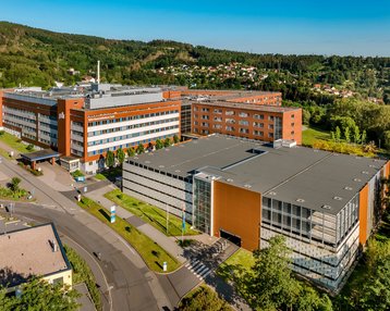 Moderne Gebäude mit orangefarbenen Fassaden und grünen Flächen, umgeben von Bäumen und Hügeln.