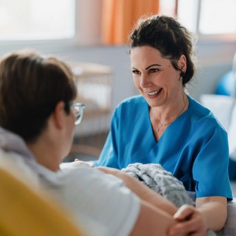 Eine Krankenschwester spricht freundlich mit einer Patientin im Krankenhaus, während sie sich auf einem Bett ausruht.